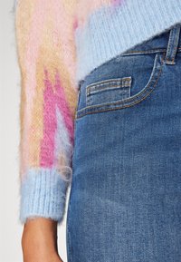 Suéter de punto con texturas difusas en rosa, naranja y azul; con puños acanalados en azul. Combina con jeans de mezclilla azul oscuro.