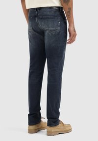 Donkerblauwe denim jeans met een recht model, subtiele vervaging, vijf zakken en zichtbare stiksels, gecombineerd met beige schoenen.