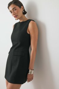 Juoda be rankovių suknelė su pritaikytu siluetu, dviem priekinėmis kišenėmis ir subtiliu siūlų apdaila; derinama su metaline apyranke.