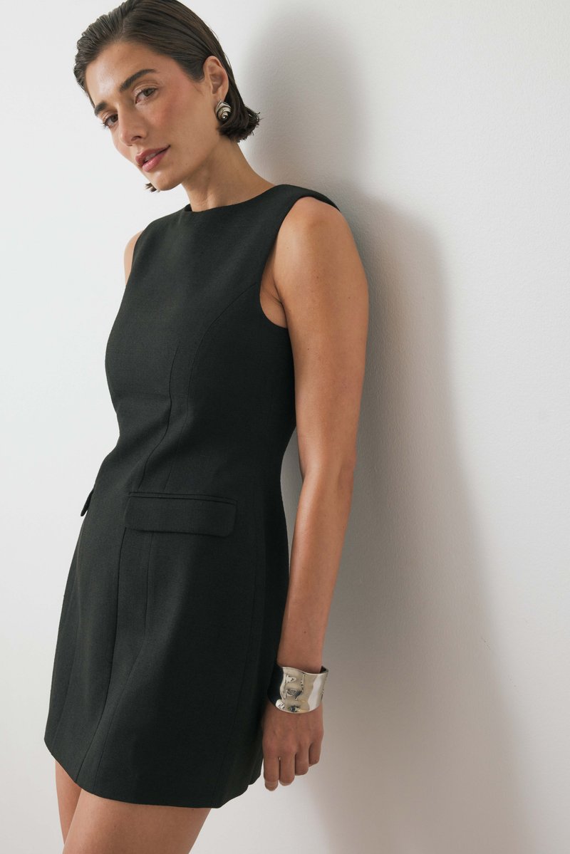 Juoda be rankovių suknelė su pritaikytu siluetu, dviem priekinėmis kišenėmis ir subtiliu siūlų apdaila; derinama su metaline apyranke.