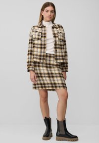 Gestreepte jas- en rokset in beige, bruin en zwart. Gelaagd stof, met een getailleerde snit. Stevige zwarte enkellaarzen met elastische zijkanten.