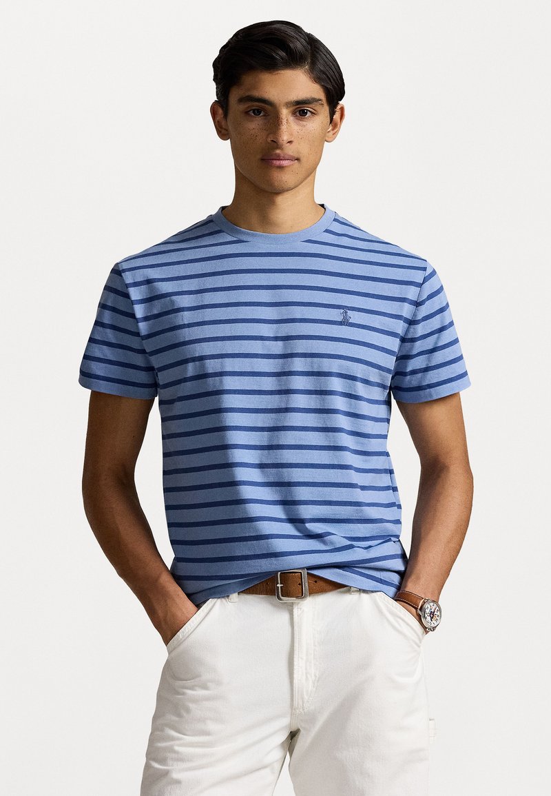 Tricou bleu cu dungi, realizat din bumbac, având guler rotund și mâneci scurte. Logo brodat pe pieptul stâng. Asortat cu pantaloni de culoare deschisă.