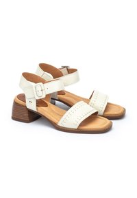 Sandalias de cuero blanco con tacones de bloque de madera, que presentan dos correas anchas y una correa para el tobillo con hebilla. Detalles de costura en las correas.