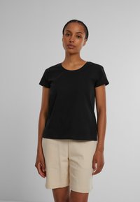 Svart bomull T-skjorte med rund hals og korte ermer, sammen med beige shorts, satt mot en ensfarget grå bakgrunn.