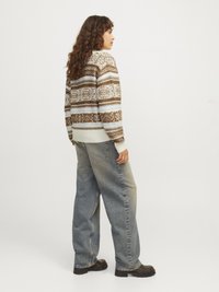 Pull en tricot avec des motifs géométriques marron, blanc et bleu ; coupe confortable avec des poignets côtelés. Associé à un jean évasé décoloré et des bottes noires.