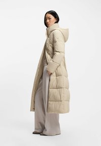 Beige pufferjacka med huva, med stickade paneler och en l�ång silhuett. Texturerat tyg och detaljer i metall.