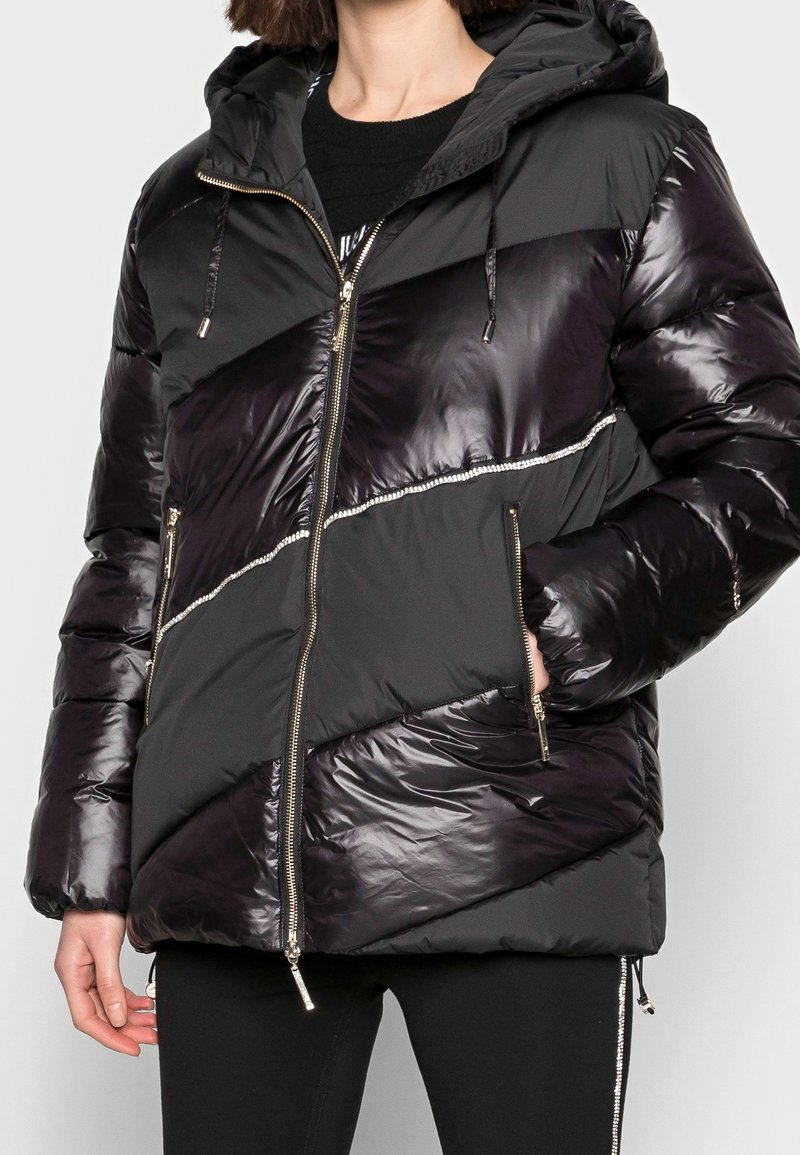 Giubbotto puffer nero con cappuccio, con pannelli diagonali lucidi e una zip argentata. Tessuto strutturato con sezioni lisce e opache.