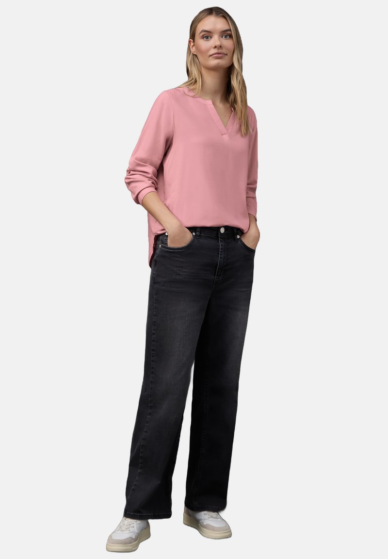Rosa Langarmbluse mit V-Ausschnitt kombiniert mit schwarzen, weiten Jeans und weißen Sneakern. Glatte Textur, lockere Passform und klassisches Design.