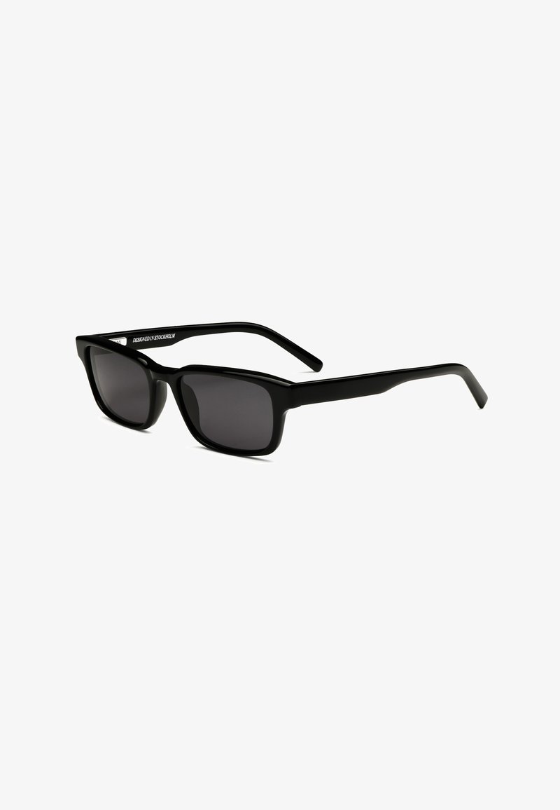 Lunettes de soleil rectangulaires noires avec des verres teintés foncés et des branches droites, légèrement inclinées vers la droite sur un fond blanc.