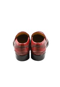 Scarpe in pelle rossa con texture liscia, retro arrotondati, suole nere e dettagli di cucitura decorativi. Nessun lacci o fibbie visibili.