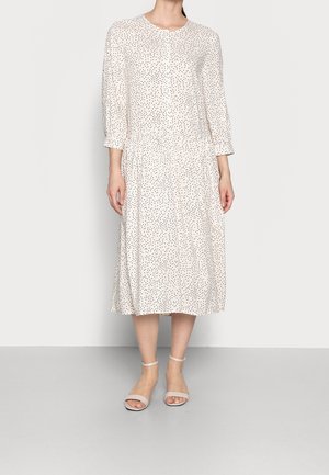 Jasnobeżowa sukienka w drobne czarne kropki, z rękawami do połowy przedramienia, okrągłym dekoltem i talią zebrana w marszczenie. Do tego miękkie, cieliste sandały na kostkę z paskiem.