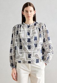 Camicia con bottoni realizzata in tessuto testurizzato, caratterizzata da un motivo geometrico in blu navy, bianco e verde. Maniche a palloncino con dettaglio arricciato sulle spalle.
