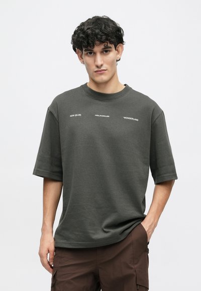 Tamno siva prevelika majica s kratkim rukavima izrađena od mekane pamuka. Ima bijeli natpis na prednjem dijelu. Ležeran kroj s okruglim izrezom.