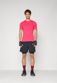 Camiseta deportiva de manga corta rosa con el logo negro de Nike, combinada con pantalones cortos negros, guantes sin dedos, zapatos negros y calcetines burdeos.