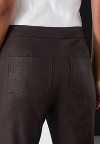 Pantaloni din piele ecologică maro cu două buzunare la spate, având o textură netedă și o croială ajustată, asortați cu un top alb cu dungi.