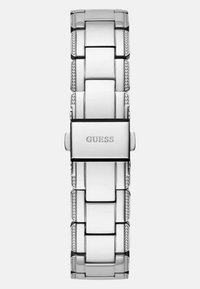 Hõbedatooni metallkell, millel on poleeritud linkide disain, sisaldab väikeseid tekstureeritud aktsente ja klambrit, millel on graveering "GUESS."