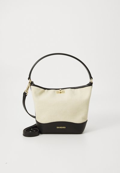 Canvas and leather handbag with a cream upper and black lower section. Features a top closure and gold-tone hardware. Adjustable strap.
