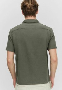 Korte mouwen, olijfgroene shirt, textuurstof, met kraag ontwerp, licht oversized pasvorm, zichtbare stikdetails op schouders en rug.