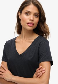 Camiseta negra de cuello en V en tejido ligero con mangas cortas, que presenta un logo sutil en el lado izquierdo del pecho y un diseño de corte relajado.
