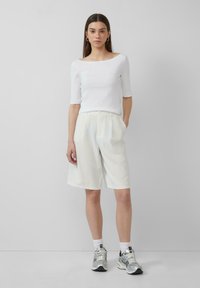 Witte geribde top met een bootnecklijn, gecombineerd met licht gestreepte shorts en zilveren sneakers. Eenvoudig ontwerp, relaxte pasvorm en neutrale kleur.