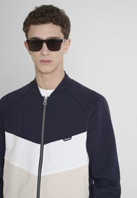 Giacca zip-up blu navy con blocchi di colore bianco e beige. Caratterizzata da un collo rotondo, maniche raglan e un piccolo logo sul davanti.