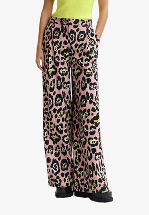 Pantaloni a gamba larga con stampa leopardata rosa, nera e gialla, indossati con scarpe chunky nere e una canotta gialla acceso.