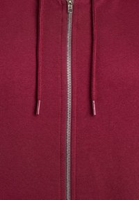 Felpa con zip color marrone bordeaux, dotata di una cerniera in metallo argentato, laccetti con estremità coordinate e una finitura in tessuto morbido e testurizzato.