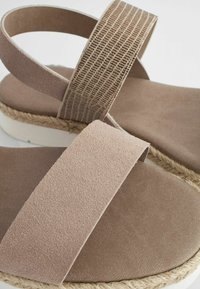 Ljusbruna sandaler med ett texturerat rem, slät mockakropp och vävd jutesula, med en vit gummibas.