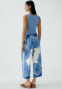 Blaues geripptes Tanktop kombiniert mit weitem blauen und weißen Blumen-Hosen. Die Hose hat ein auffälliges Blumenmuster und eine glatte Textur.