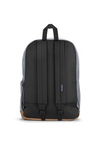 Sac à dos avec un extérieur en tissu gris, des bretelles rembourrées noires et un fond en cuir marron. Comprend une poignée de transport sur le dessus et des poches latérales.