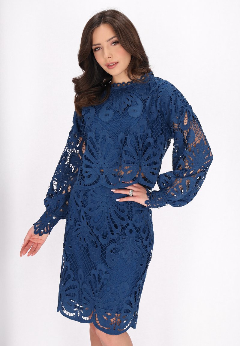 Navyblaues Spitzenkleid mit floralem Ausschnitt, langen Ärmeln und rundem Halsausschnitt, körperbetonter Silhouette und knielangem Saum.