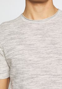 Camiseta de textura gris claro con cuello redondo. Tela suave, mangas cortas, con un sutil patrón horizontal y bordes limpios.