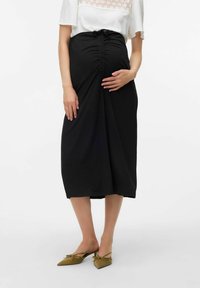 Gonna nera premaman con arricciature laterali e dettaglio con fiocco in vita. Tessuto morbido, design alla caviglia, abbinata a scarpe flat verde oliva a punta.