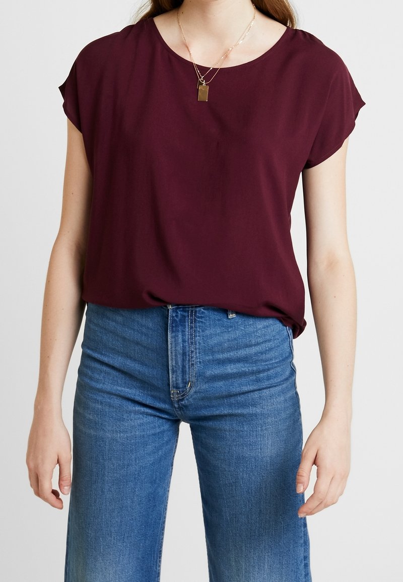 Burgundy kortærmet bluse, letvægtsstof, afslappet pasform, rund halsudskæring. Sammen med højtaljede lyseblå denim jeans.