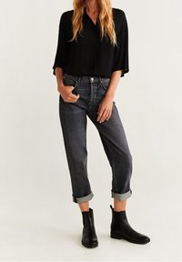 Schwarzes kurzärmliges Hemd mit Knöpfen, kombiniert mit grauen Jeans mit umgeschlagenen Säumen und schwarzen Stiefeletten, die eine glatte Textur und ein klassisches Design aufweisen.
