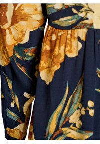 Bloemenjurk met een marineblauwe achtergrond, grote gele en oranje bloemen, groene bladeren en een gestructureerde stof. Voorzien van plooidetails.