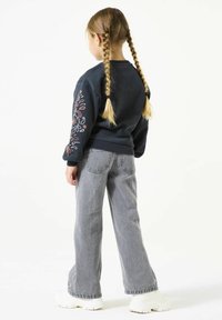 Felpa blu scuro con ricami floreali sulla manica sinistra, abbinata a jeans a campana grigi chiari e sneakers bianche con piattaforma.