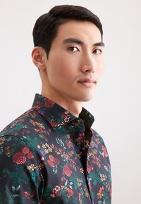 Camicia a maniche corte con bottoni, su sfondo nero, con motivi colorati di fiori e foglie, in tessuto morbido e colletto classico.