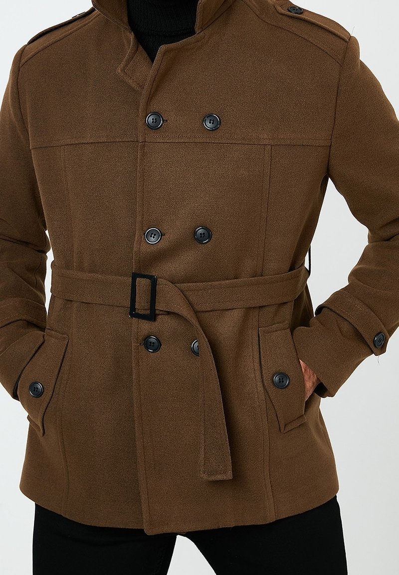 Cappotto in misto lana marrone con chiusura a doppio petto con bottoni, vita con cintura, spalline, tasche laterali e collo alto.