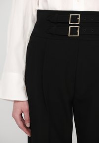 Pantaloni neri a vita alta con due ampie passanti per cintura, dettagli con doppia fibbia e una texture di tessuto liscia e su misura.