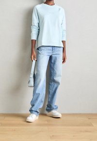 Sudadera de color azul claro con puños y dobladillo acanalados, combinada con unos vaqueros de corte holgado de color azul claro. Zapatillas blancas y un bolso de hombro azul claro completan el conjunto.