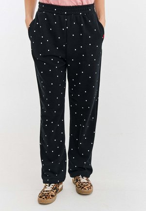 Czarne dresy w białe kropki, elastyczny pas, boczne kieszenie, luźny krój, zestawione z butami w zwierzęcy print.