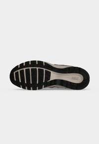 Σόλα ενός παπουτσιού Nike για τρέξιμο με μαύρο και μπεζ πέλμα, ορατά πρότυπα πρόσφυσης και το λογότυπο της Nike κοντά στην περιοχή της φτέρνας.