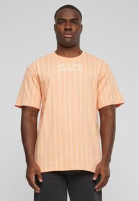 T-shirt rayé pêche avec des lignes verticales blanches. Présente un col rond et un logo "KANI" en blanc sur la poitrine. Manches courtes.