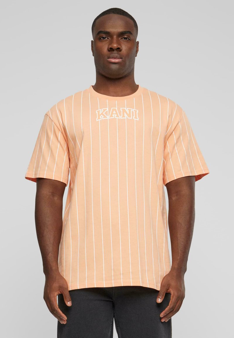 T-shirt rayé pêche avec des lignes verticales blanches. Présente un col rond et un logo "KANI" en blanc sur la poitrine. Manches courtes.