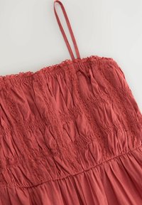 Robe couleur rouille avec corsage froncé et accents en dentelle. Présente des bretelles fines et une jupe fluide. Tissu doux et léger.