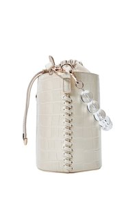 Sac cylindrique beige avec motif crocodile, détail cousu, fermeture par cordon en tissu et porte-clés transparent à perles attaché.