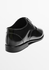 Chaussure habillée en cuir noir avec une finition polie, un design à lacets, un bout arrondi et une semelle en caoutchouc plate. Présente des détails de couture subtils.