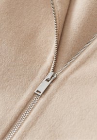 Gros plan sur un tissu en laine beige avec une fermeture éclair métallique argentée partiellement ouverte.