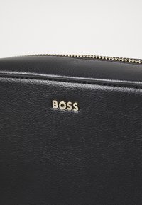 Borsa in pelle nera con superficie texturizzata, caratterizzata da una zip dorata e un logo "BOSS" dorato. Finitura liscia con cuciture minime.